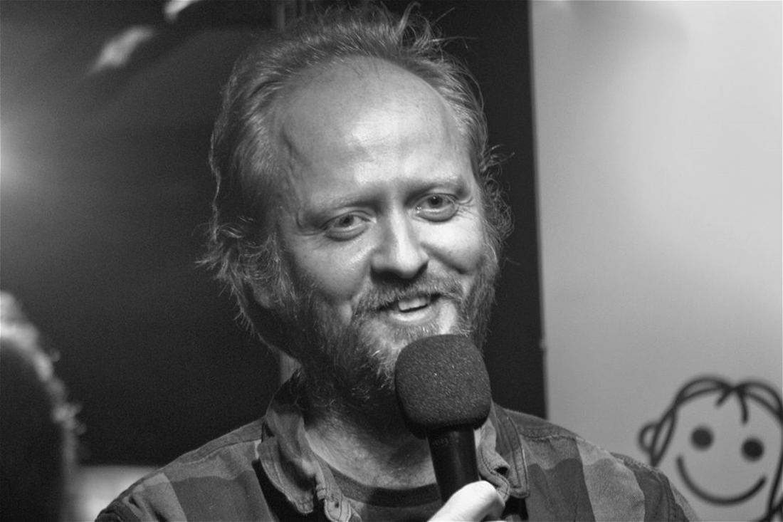 Adam Riley performing stand-up, holding a microphone